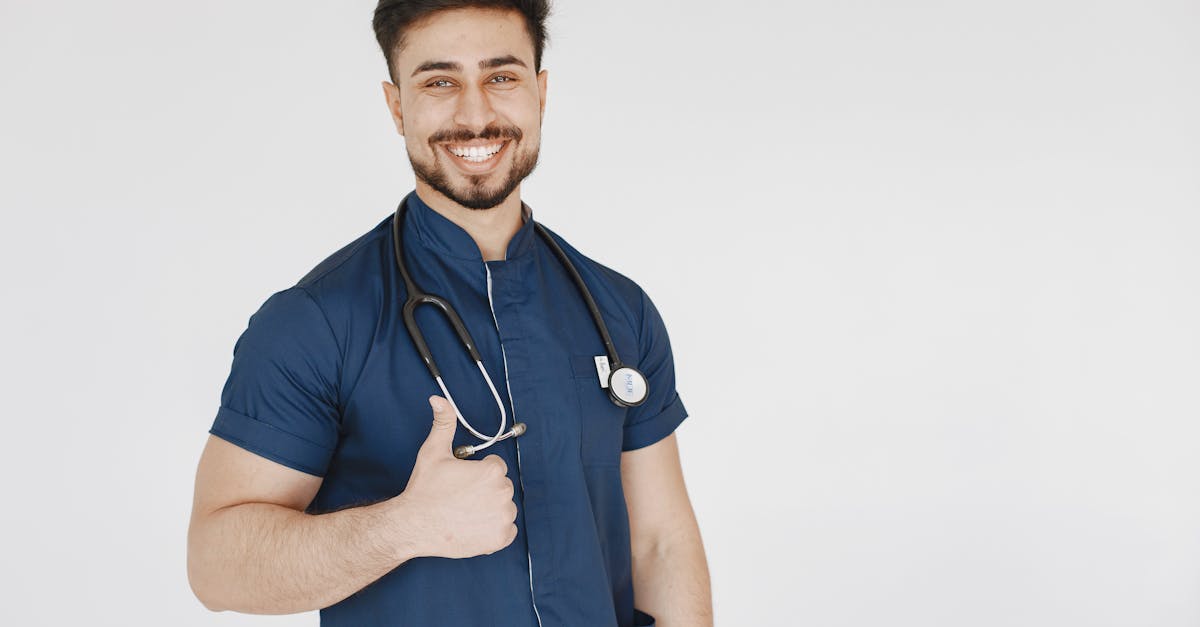 Confident male doctor in blue scrubs with a stethoscope smiling and giving a thumbs up.